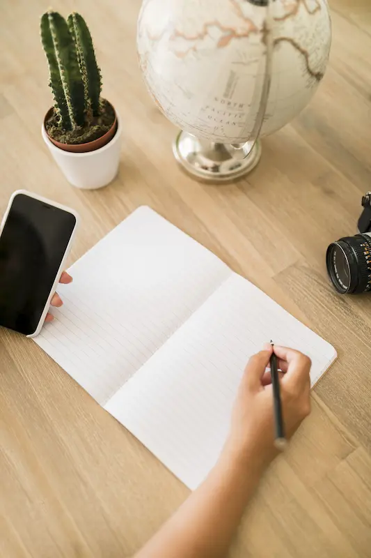 Hand writing in a notebook with globe and phone, representing multilingual content creation